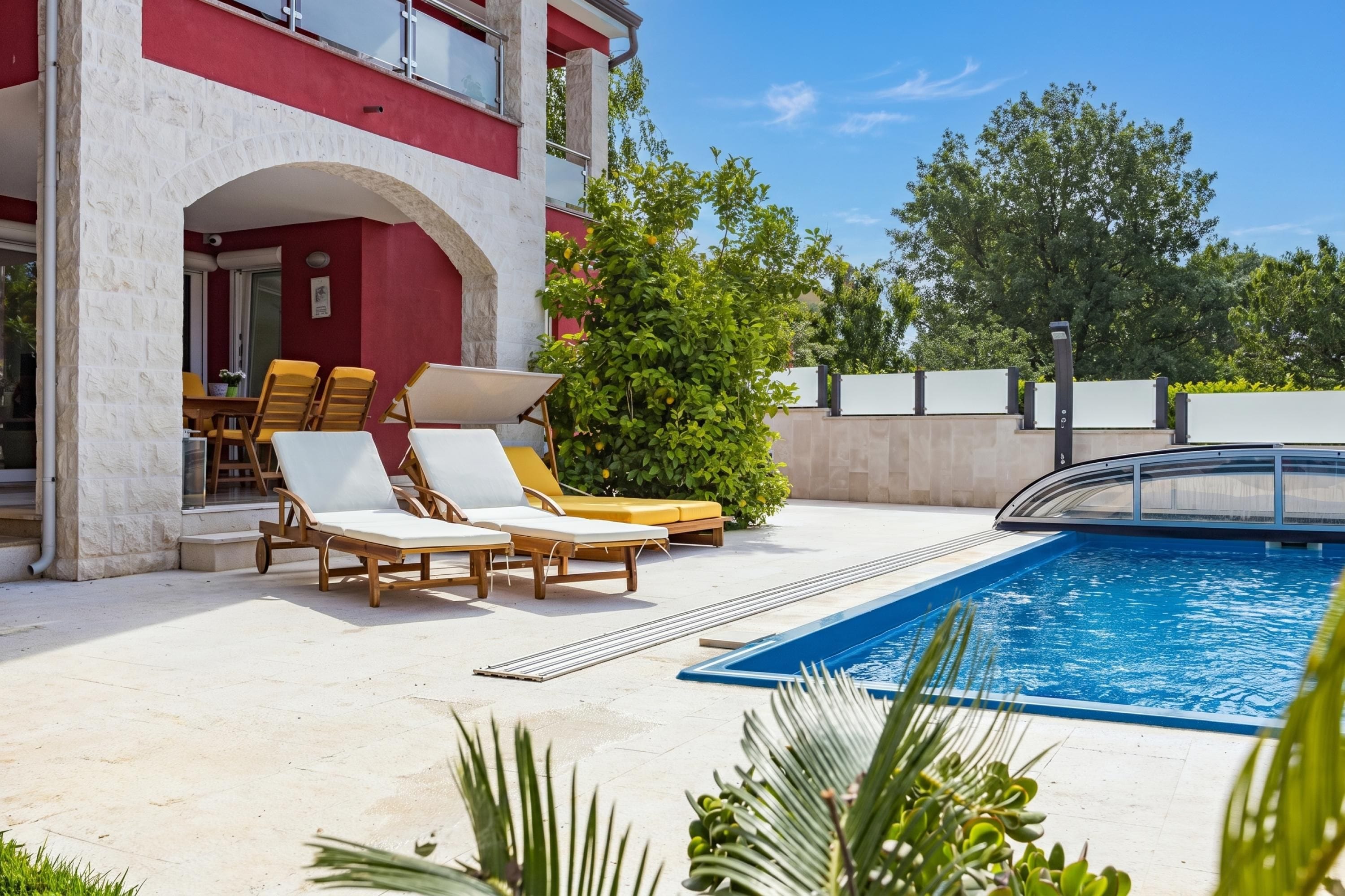 A pool area with lounge chairs, a small table, and a view of a building with red and white walls.