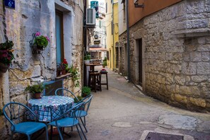 A narrow street with a table and chairs set up outside a building, surrounded by stone walls and potted plants. - Apartment Ayni With Private Pool (Umag)
