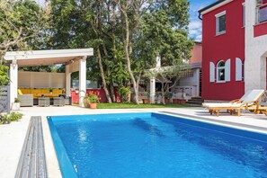 A swimming pool with a wooden deck, lounge chairs, and a covered seating area. - Apartment Ayni With Private Pool (Umag)