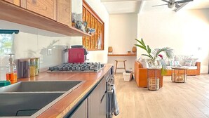 A modern kitchen with wooden cabinets, a built-in stove, and a dishwasher. There is a dining area with a table and chairs, and a large window providing natural light.