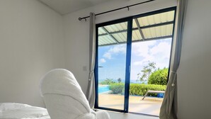 A bedroom with a large bed, a view of the outdoors through a sliding glass door, and a ceiling fan.