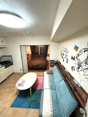 A compact living space with a kitchenette, a sofa, a small table, and a wall decorated with family photos and a globe. - Sapporo East2 Stay minpaku (Sapporo)