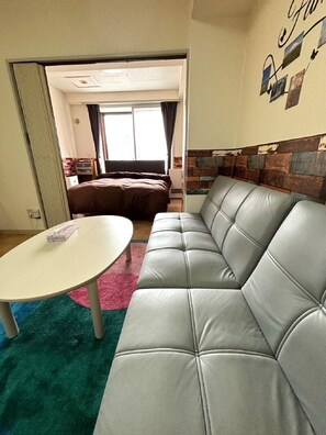 A modern living room with a grey leather sofa, a white table, and a colorful rug. - Sapporo East2 Stay minpaku (Sapporo)