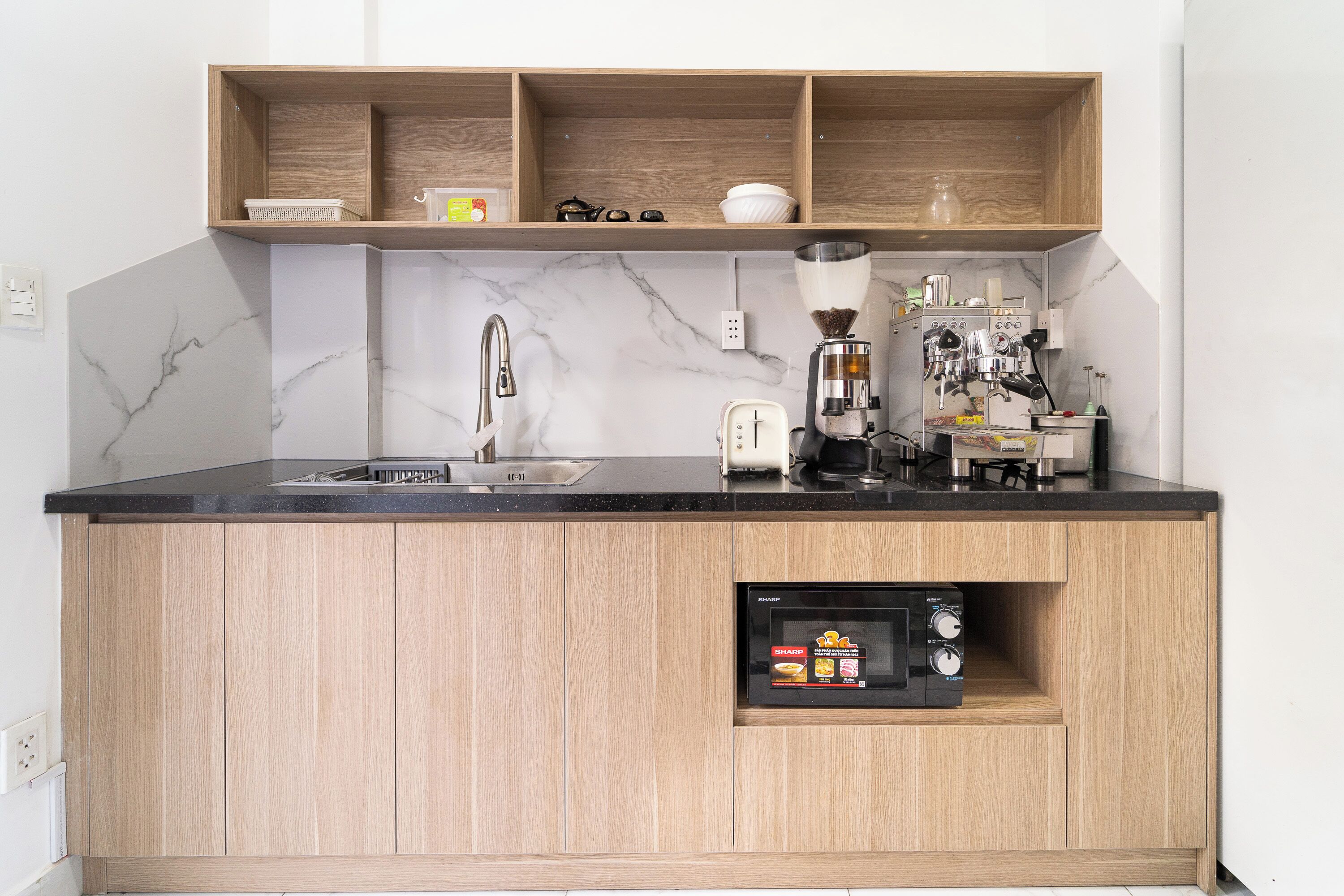 A kitchen with a marble backsplash, wooden cabinets, a built-in microwave, and a coffee machine.