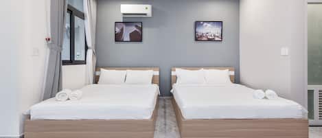 Una habitación de hotel moderna con dos camas, un ventanal con cortinas, un equipo de aire acondicionado y dos cuadros enmarcados en la pared.