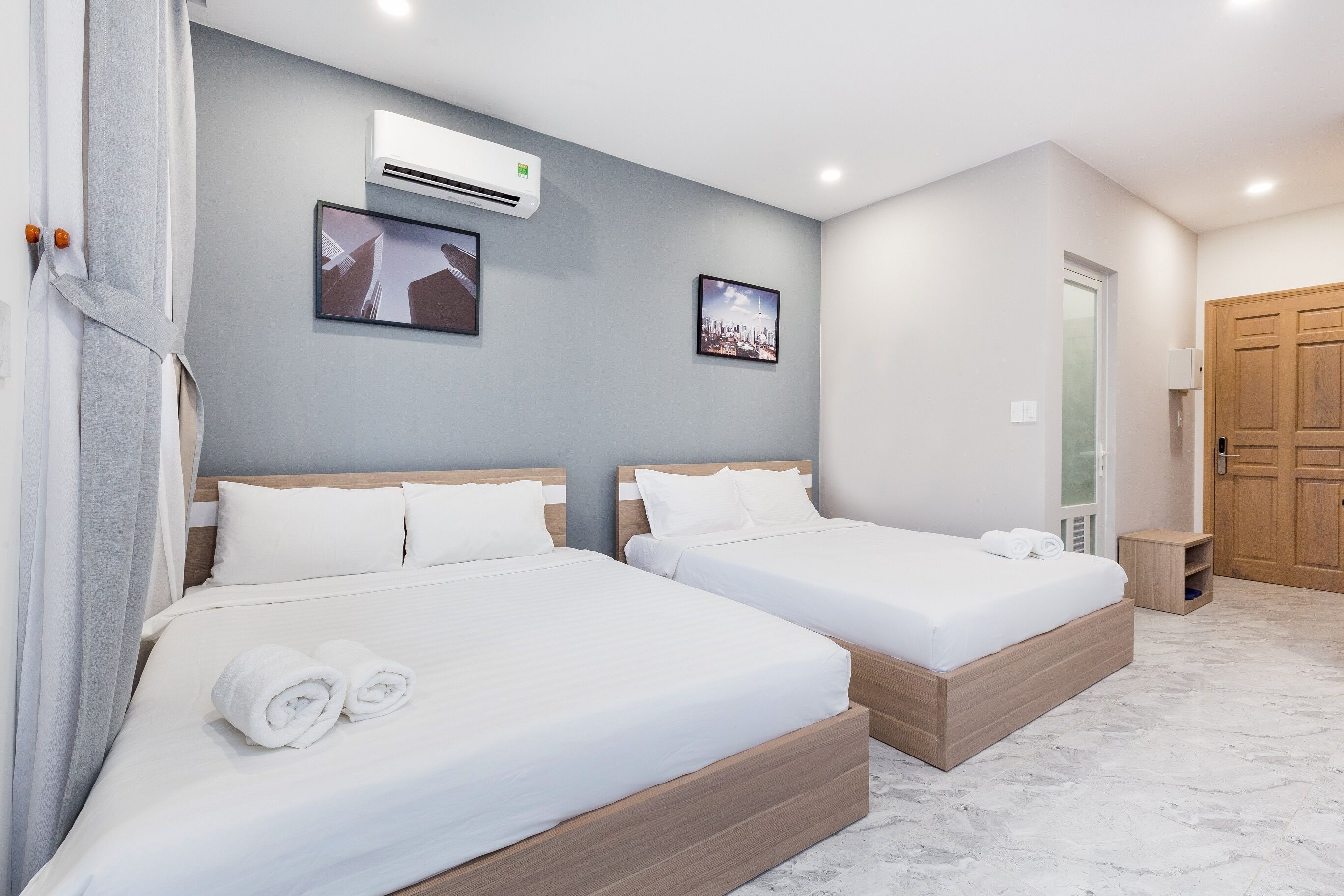 A modern hotel room with two beds, a wooden headboard, a small bedside table, and an air conditioning unit on the wall.