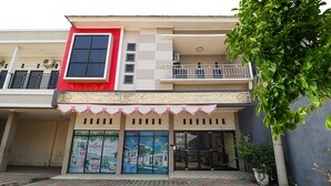 A two-story building with a red and white facade, a balcony with a railing, and a large entrance with glass doors. - SPOT ON 3859 Sweet Candy 2NearResinda park mall (Karawang)