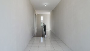 A hallway with white walls and tiled floors, leading to a room with a window and a door. - SPOT ON 3859 Sweet Candy 2NearResinda park mall (Karawang)