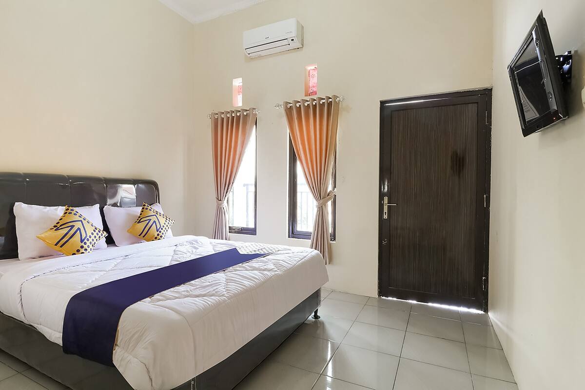 Un dormitorio con cama, cortinas, una puerta y un televisor montado en la pared.