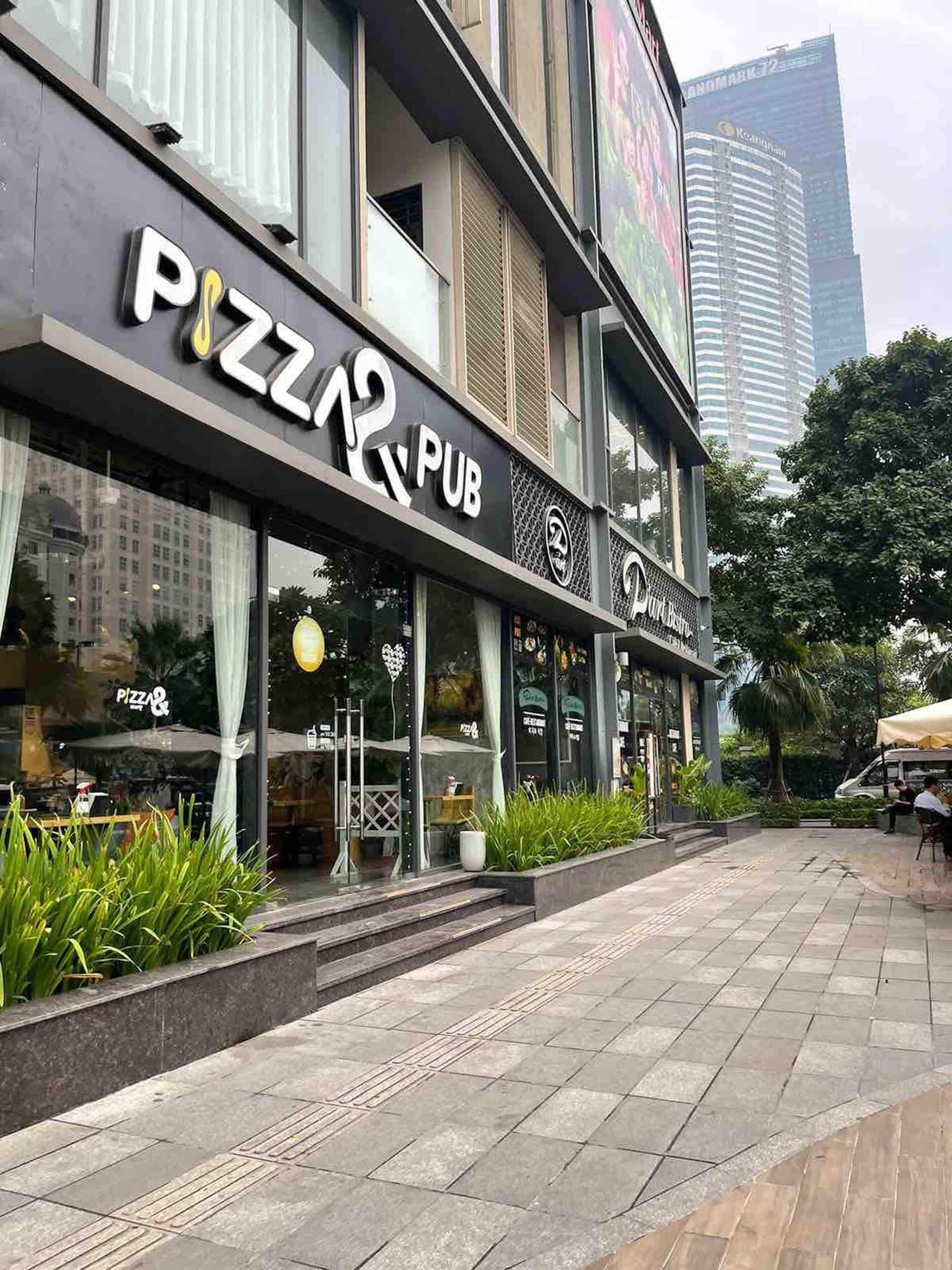 A building with a 'PIZZA PUB' sign, outdoor seating, and a view of a tall building in the background.