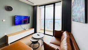 Una sala de estar moderna con una televisión de pantalla plana, un sofá, una mesita redonda y una ventana con vistas a la ciudad.
