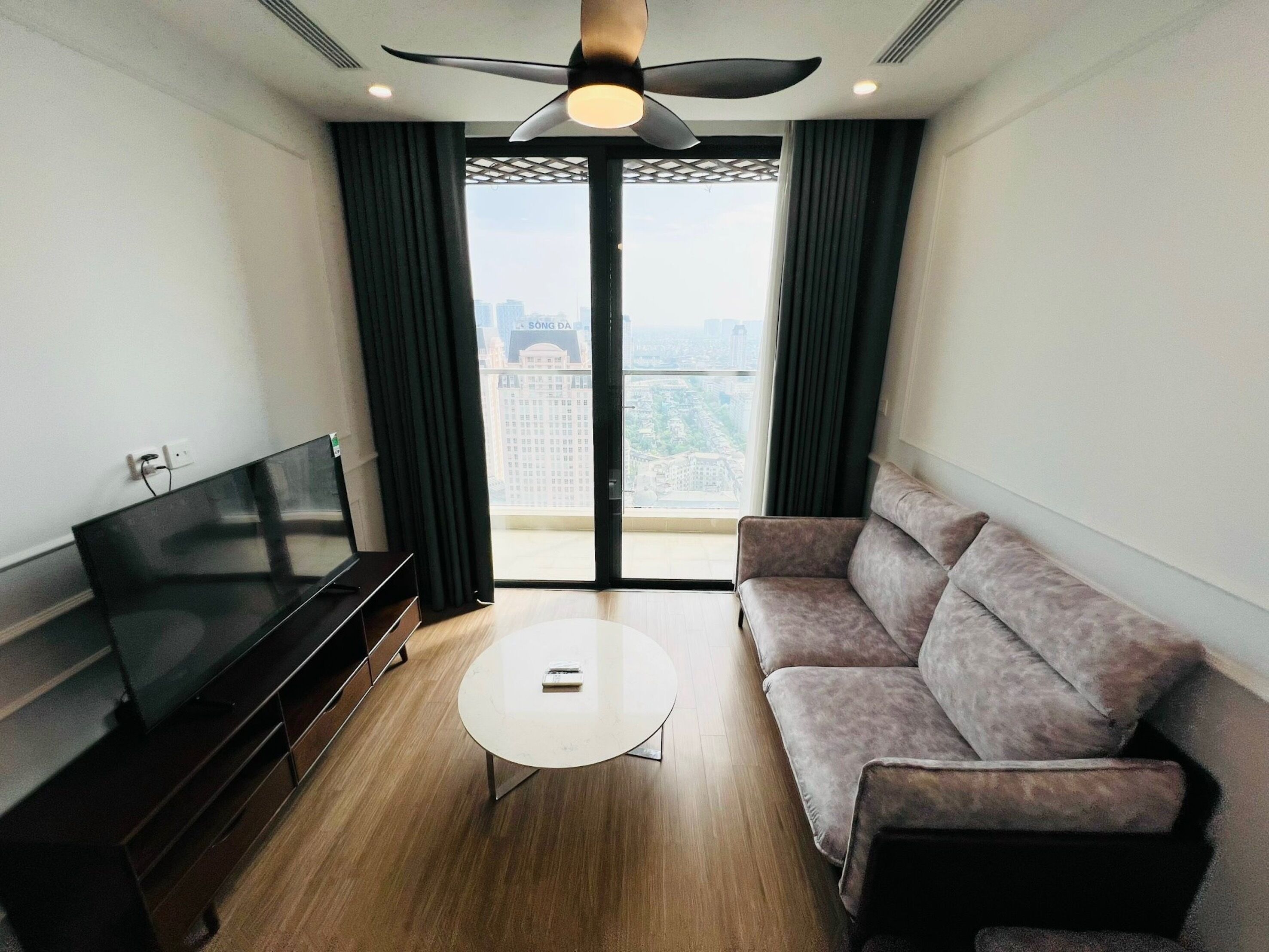 A modern living room with a flat-screen TV, a sofa, a coffee table, and a ceiling fan.