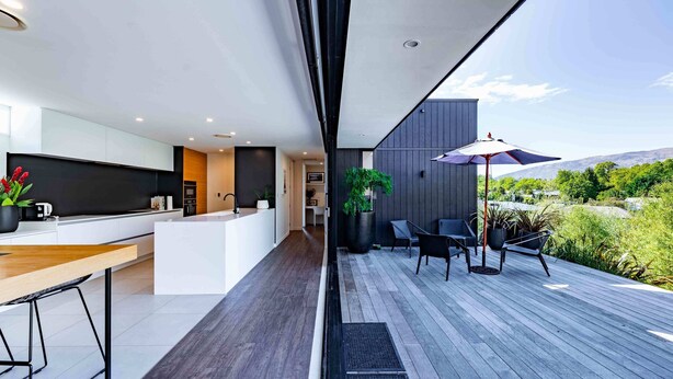A modern kitchen with a wooden countertop and bar stools, a dining area with a table and chairs, and a patio with a table, chairs, and an umbrella.