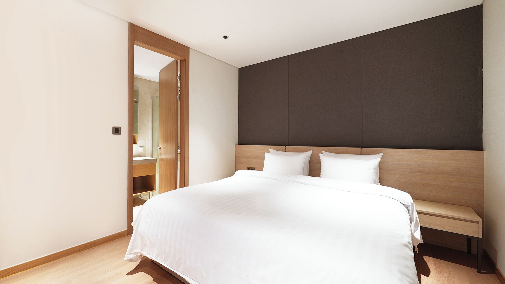 A modern bedroom with a large bed, a wooden headboard, and a built-in bench.
