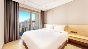 A hotel room with a large bed, a wooden headboard, a bedside table, and a view of the city through large windows. - Dominiclava Sokco (Sokcho)