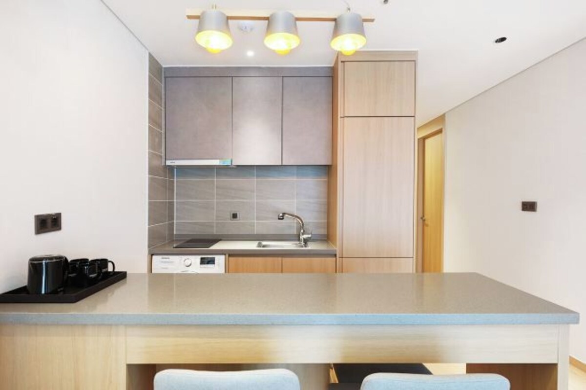 A modern kitchen with a central island, grey cabinets, and a wooden door.