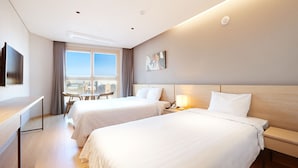 A hotel room with two beds, a desk, a chair, a TV, and a window with a city view. - Dominiclava Sokco (Sokcho)