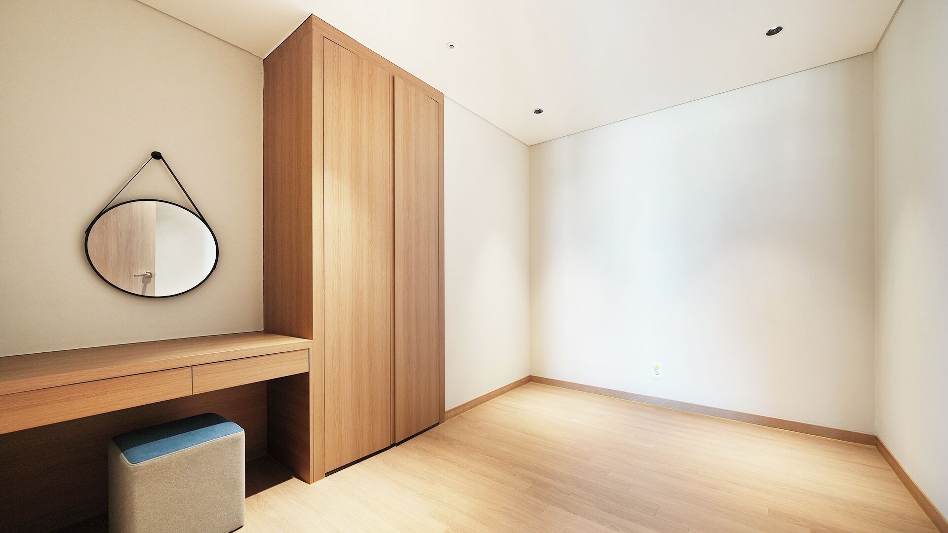 A minimalist room with a wooden wardrobe, a round mirror, and a bench.