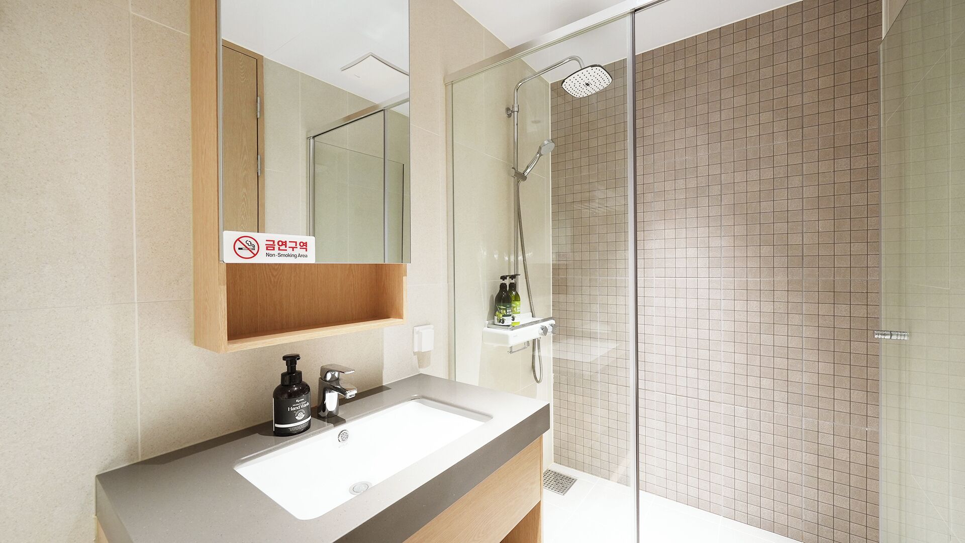 A modern bathroom with a glass shower enclosure, a sink with a soap dispenser, and a non-smoking sign.