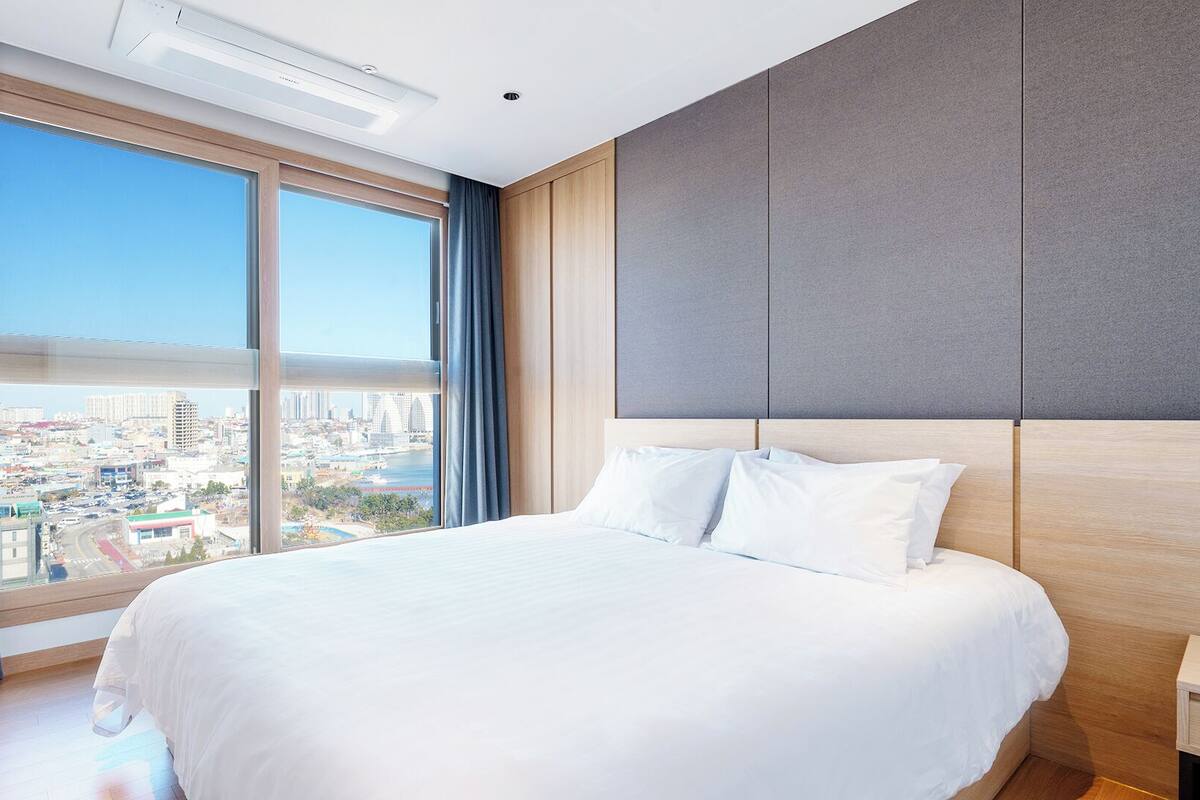 A modern hotel room with a large bed, a view of a cityscape, and a large window with curtains.