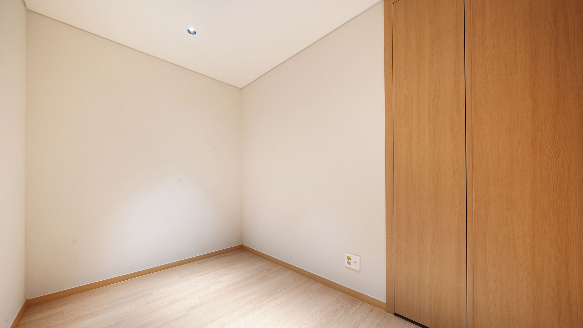 A room with a wooden wardrobe, a light-colored floor, and a recessed ceiling light.