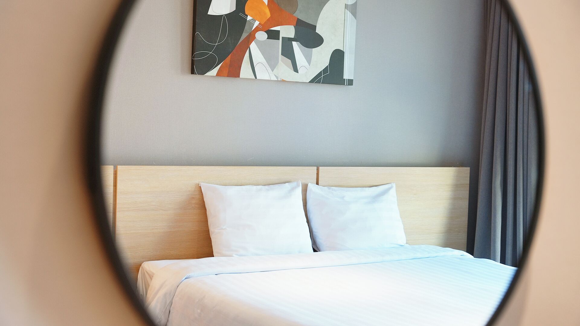 Una habitación de hotel con cama, ropa de cama blanca, cabecero de madera y un cuadro abstracto moderno en la pared.