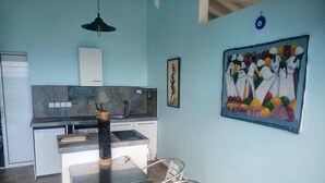 Cocina compacta con comedor, diseño moderno que incluye un protector contra salpicaduras de mármol, una lámpara colgante y un cuadro abstracto y colorido en la pared.