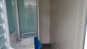 Un baño con lavamanos blanco, espejo y zona de ducha.