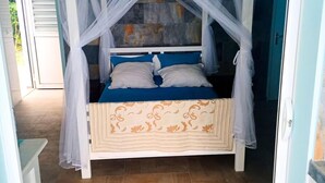 Una cama con dosel, una colcha estampada y vista al exterior por una puerta abierta.