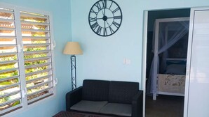 Una habitación con sofá, una mesa de centro de madera, un reloj de pared, una ventana con persianas y una cama con dosel.