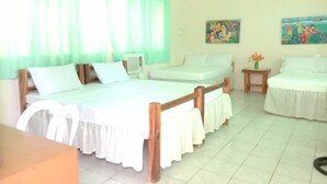 A hotel room with a bed, a chair, a small table, and a window with curtains. There are paintings on the wall.