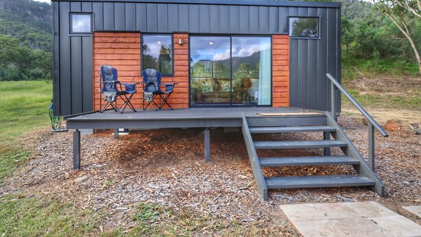 Une cabane moderne dotée d’une terrasse, de deux chaises et d’une table.