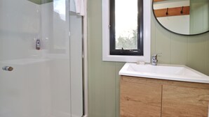 Une salle de bain avec une baignoire blanche, un meuble-lavabo en bois, un miroir rond et une fenêtre.