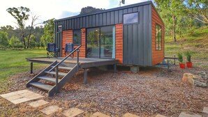 Une cabane moderne dotée d’une terrasse, de grandes fenêtres et offrant une vue sur la forêt environnante.