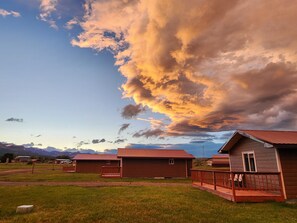 A row of wooden cabins with a metal roof, set against a backdrop of a cloudy sky.