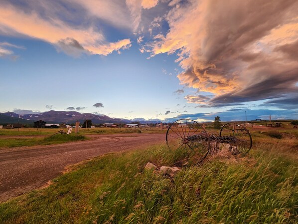 A rural landscape with a dirt road, grassy fields, and a metal structure.