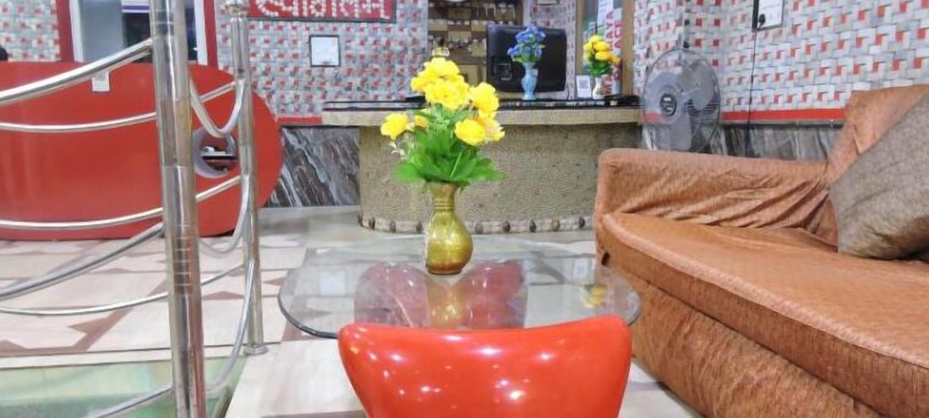 A reception area with a glass table, a vase with yellow flowers, a red sofa, and a red counter. - HOTEL MAHAMAYA PALACE (Deoghar)