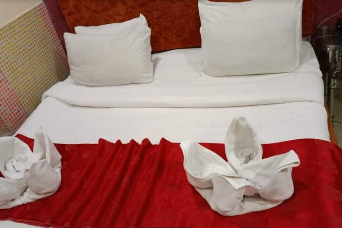 A hotel room with a neatly made bed, white bedding, and a red accent on the bedspread.