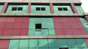 A multi-story building with a grid of windows and a red and green facade. - HOTEL MAHAMAYA PALACE (Deoghar)