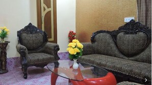 A living room with two ornate armchairs, a glass coffee table, and a vase with yellow flowers. - HOTEL MAHAMAYA PALACE (Deoghar)