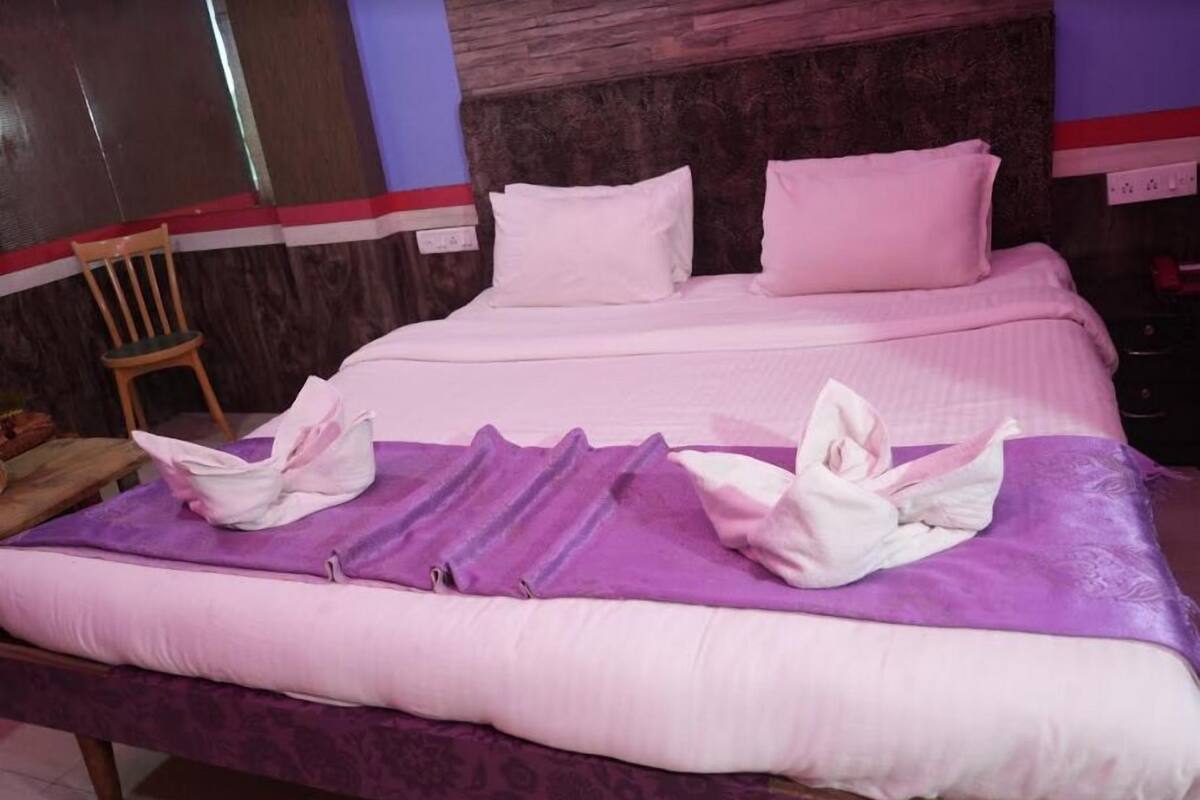 A neatly made bed with a purple blanket and white pillows, a wooden chair, and a wooden headboard.