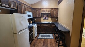 Una cocina compacta con armarios de madera, un refrigerador blanco, una estufa y un microondas.