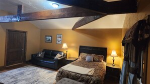 Un dormitorio con una cama, un sofá de cuero negro, una puerta de madera y dos lámparas de noche.