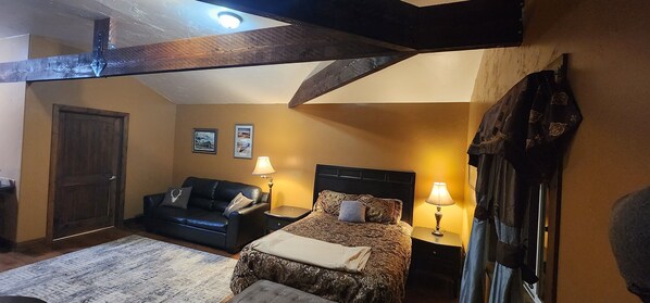 A bedroom with a bed, a black leather sofa, a wooden door, and two bedside lamps.