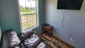 Una habitación con ventana, un televisor de pantalla plana en la pared, un sofá de cuero y una pequeña mesa de madera con un ordenador portátil.