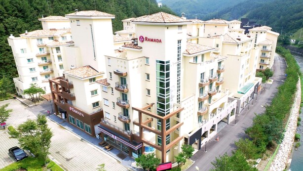 Un hotel de varios pisos con balcones, zona de estacionamiento y vistas al río.