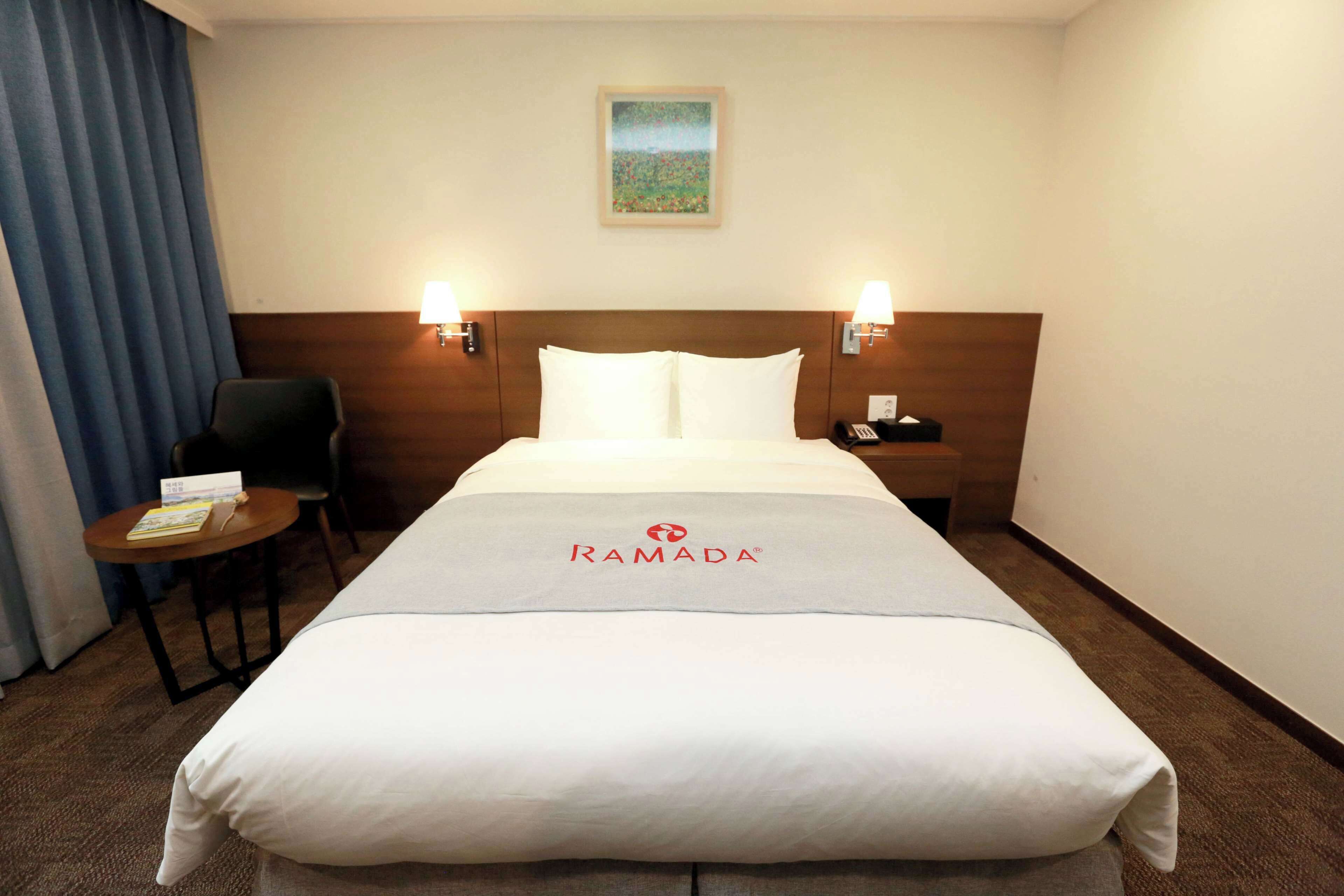 A hotel room with a large bed, two bedside tables with lamps, a small table with a chair, and a painting on the wall.