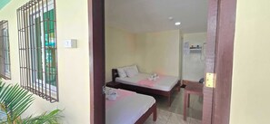Une chambre avec deux lits, une petite table et une fenêtre avec des barreaux en métal.