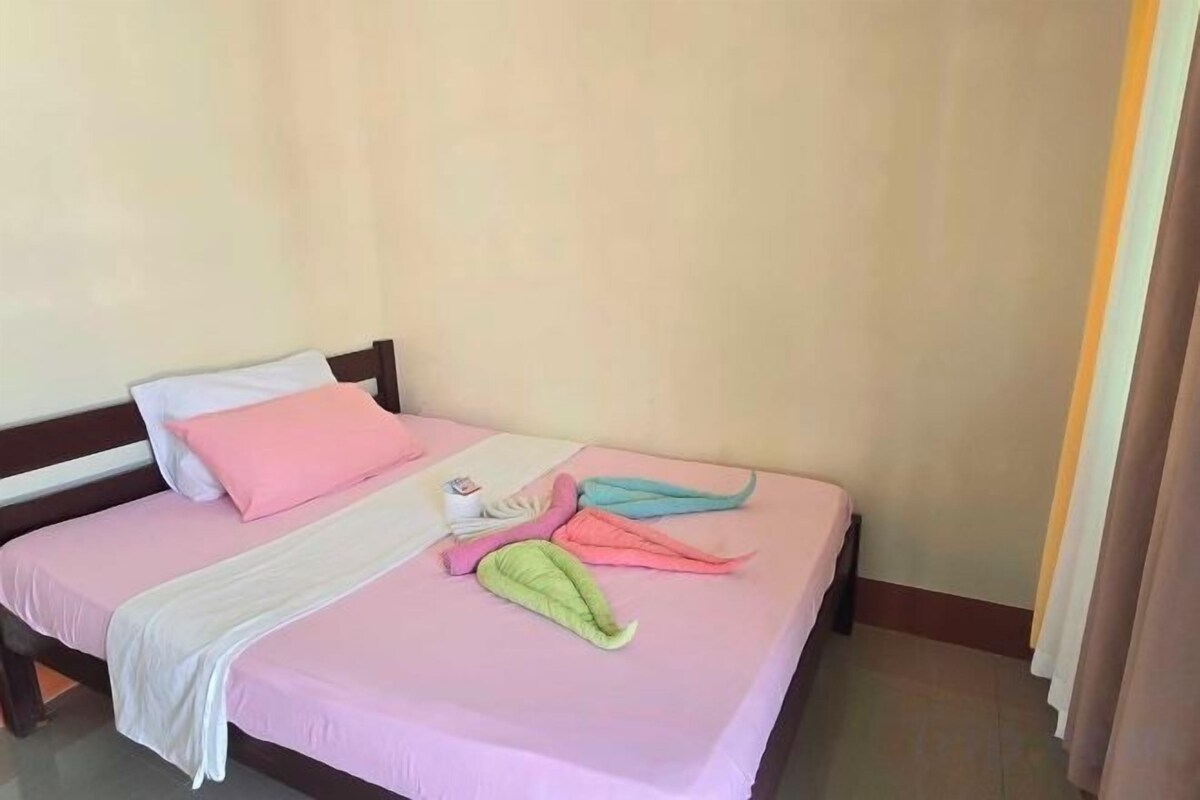 A bed with a pink bedspread, a white blanket, and a green towel.