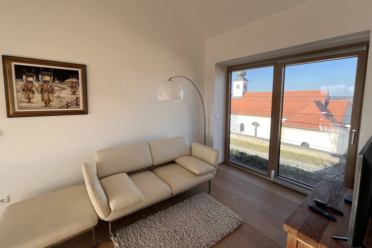 A modern living room with a beige sofa, a floor lamp, and a large window with a view of buildings.